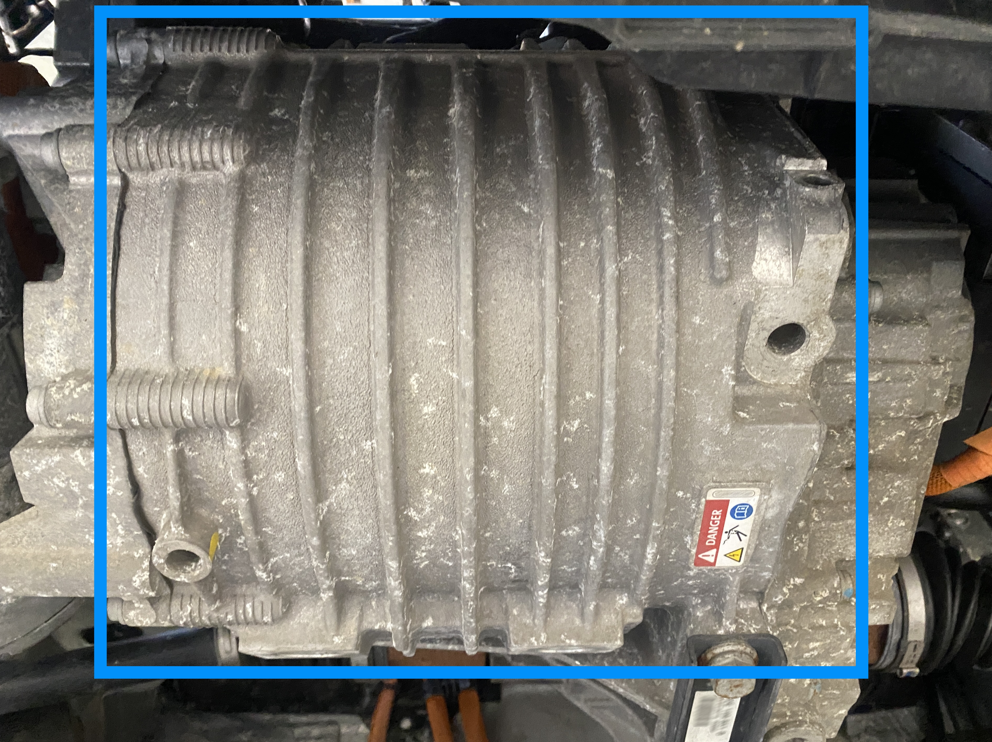 Electric motor of an electric vehicle in the underbody, with housing ribs for cooling and high-voltage warning labelling.