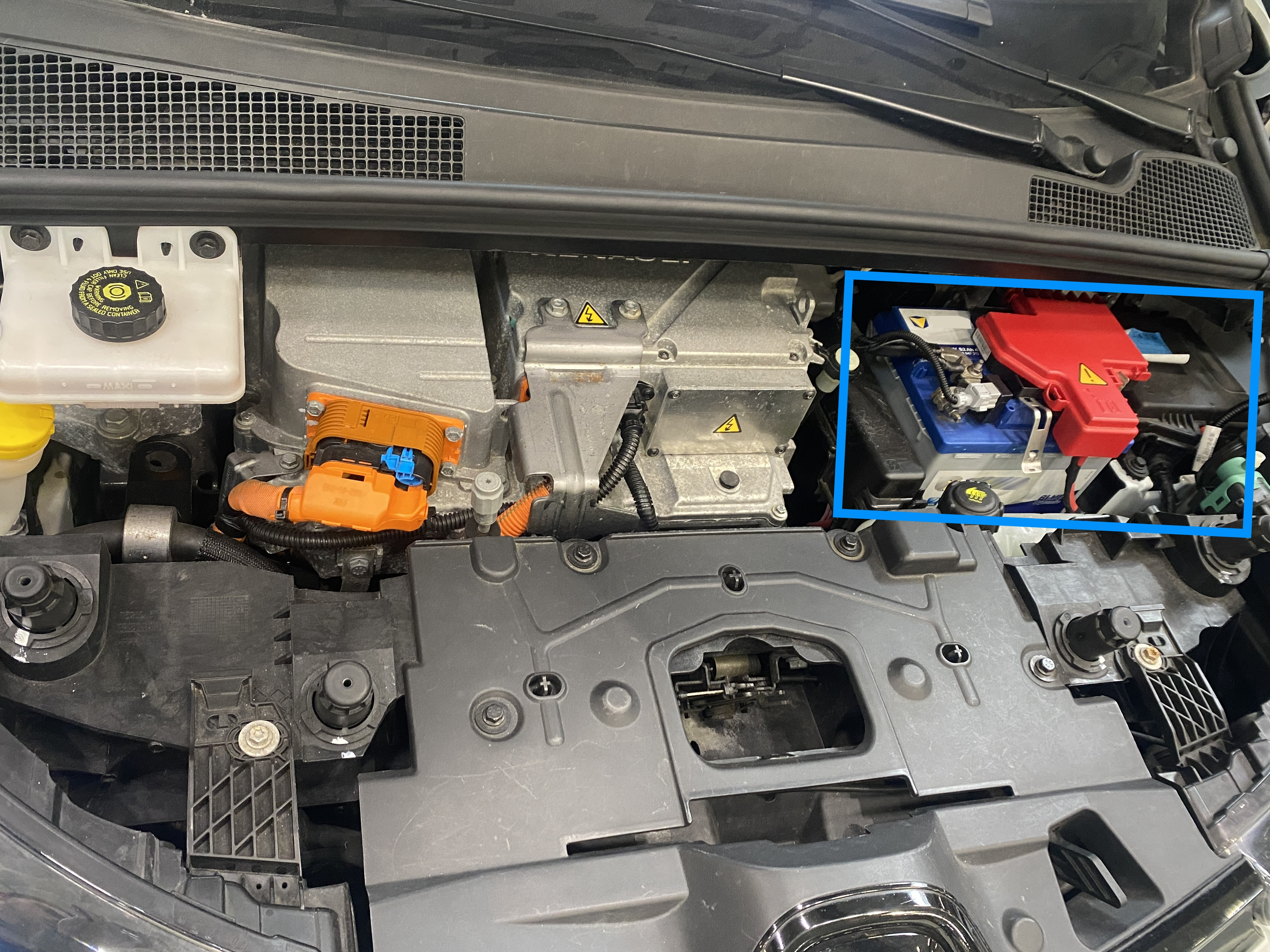 Motor compartment of an electric vehicle with visible high-voltage components and highlighted 12 V battery, supplying the low-voltage vehicle electrical system for control units and comfort functions.