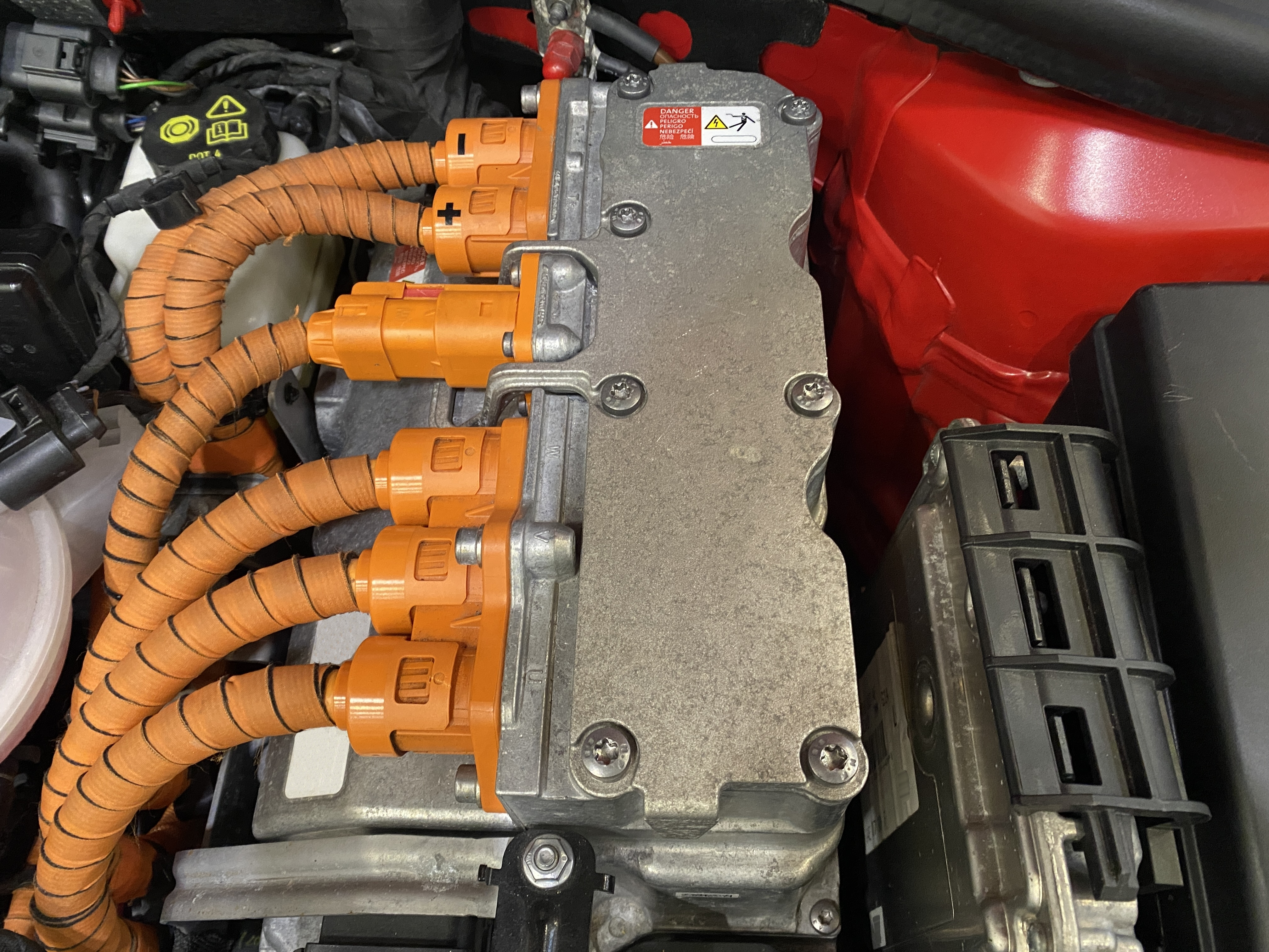 Power electronics of an electric vehicle with orange high-voltage cables and warning labelling in the motor compartment.
