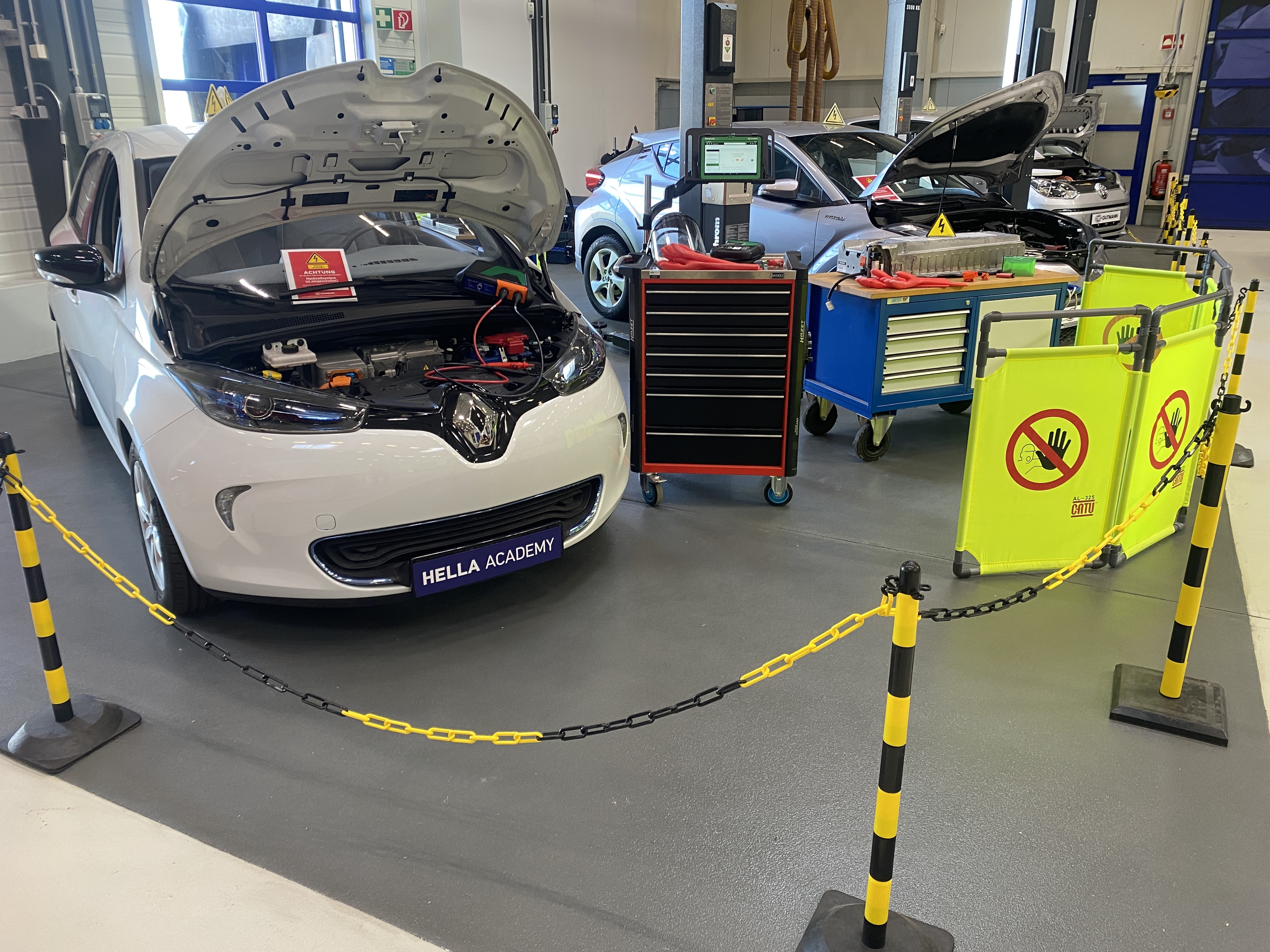 HELLA Academy high-voltage training area with locked electric vehicle, open motor compartment, diagnostic equipment and personal protective equipment to safely work on the high-voltage system.